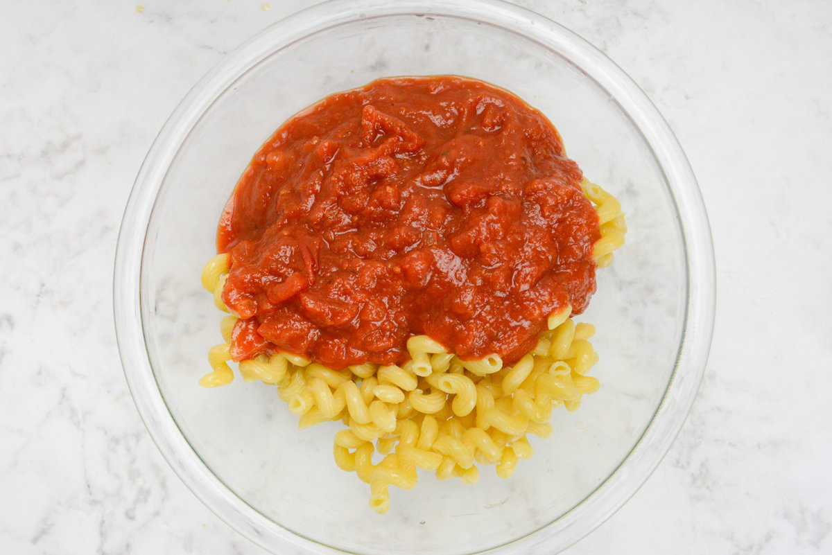 A large mixing bowl with the drained pasta and marinara poured on top but unmixed.