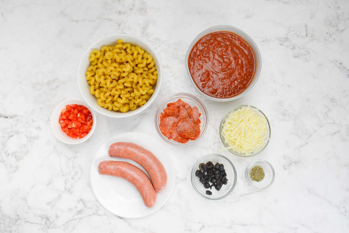 All of the ingredients to make pizza casserole in various sized bowls.