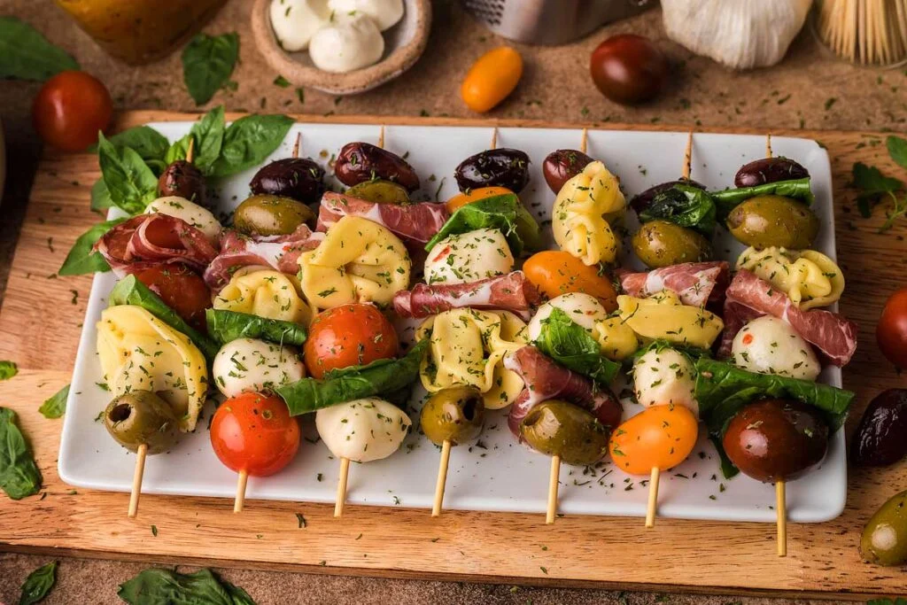 Antipasto skewers on a serving tray on a wooden board on a table.