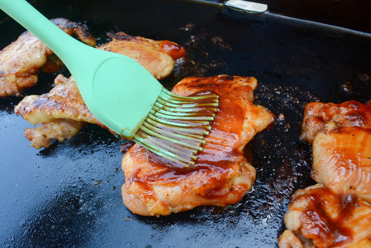 Close up of a green pastry brush adding sauce to the cooked chicken thigh 