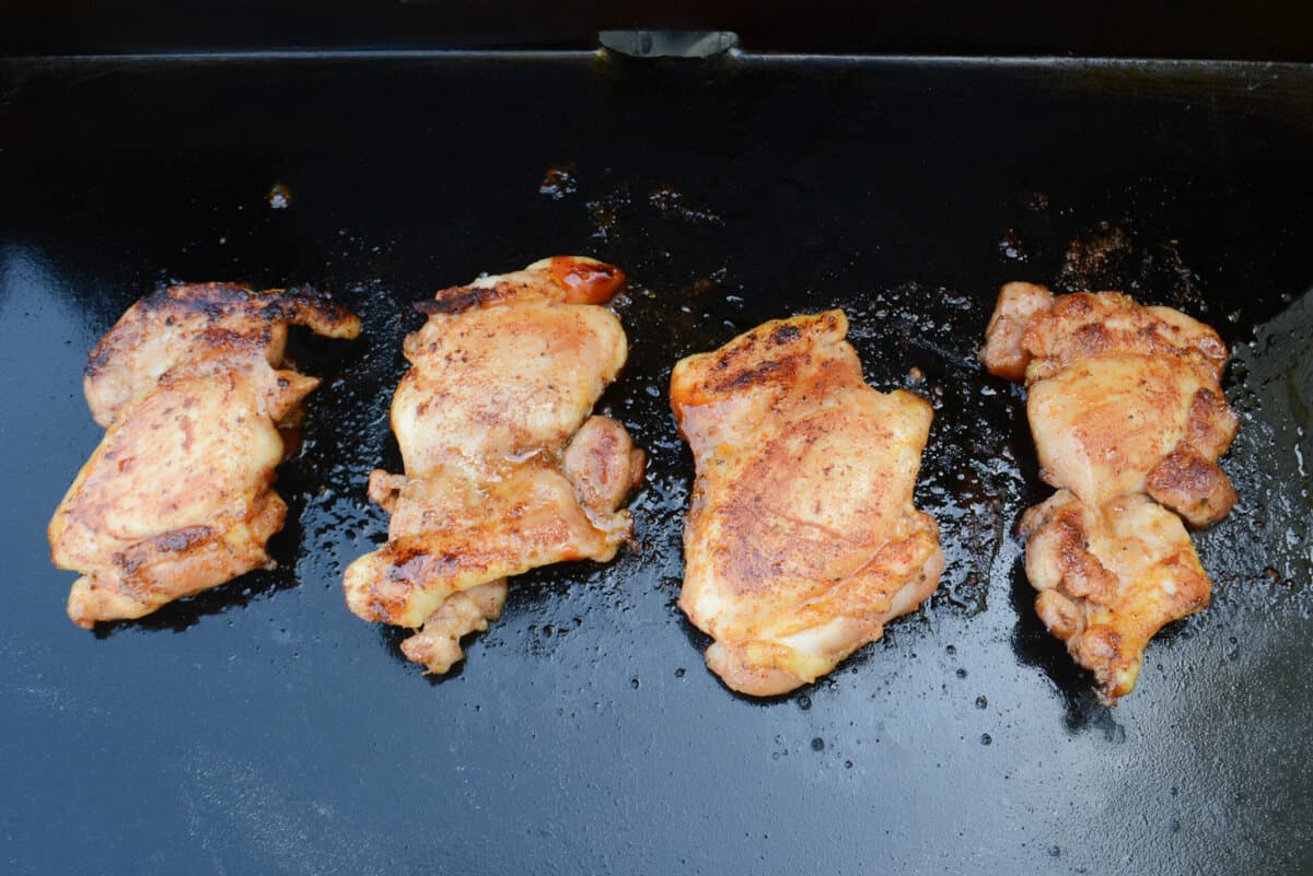 Four chicken thighs on the Blackstone after being flipped. They are lightly browned