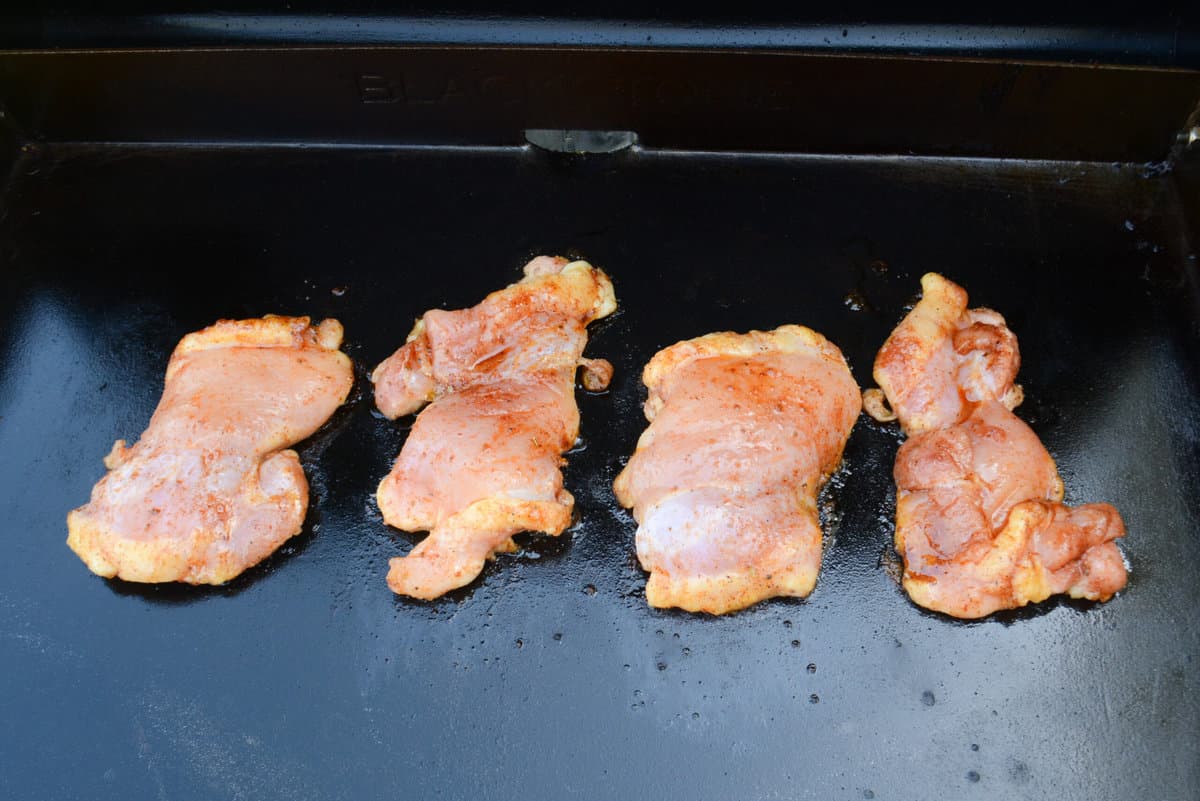 Four raw chicken thighs sit on the griddle