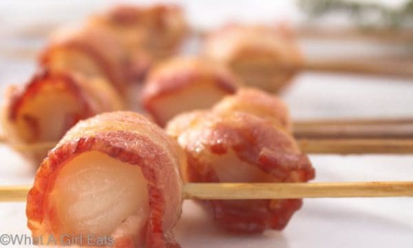 Bacon Wrapped Scallops on skewers on a plate.