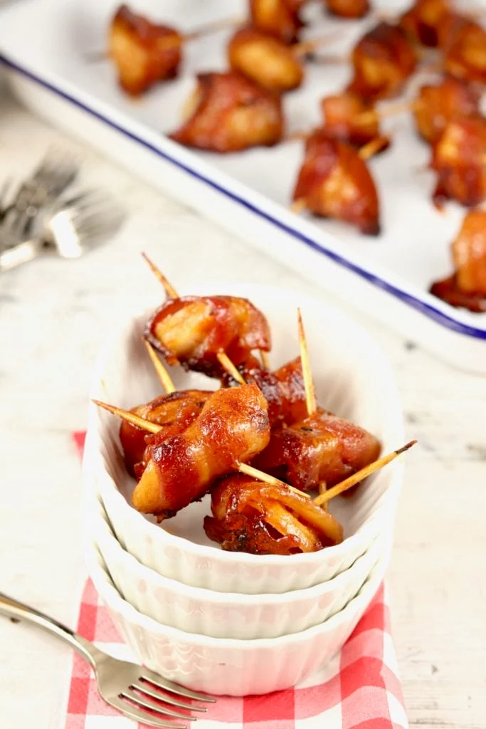 Bacon Wrapped Water Chestnuts in stacked bowls on a table on a napkin with a fork.