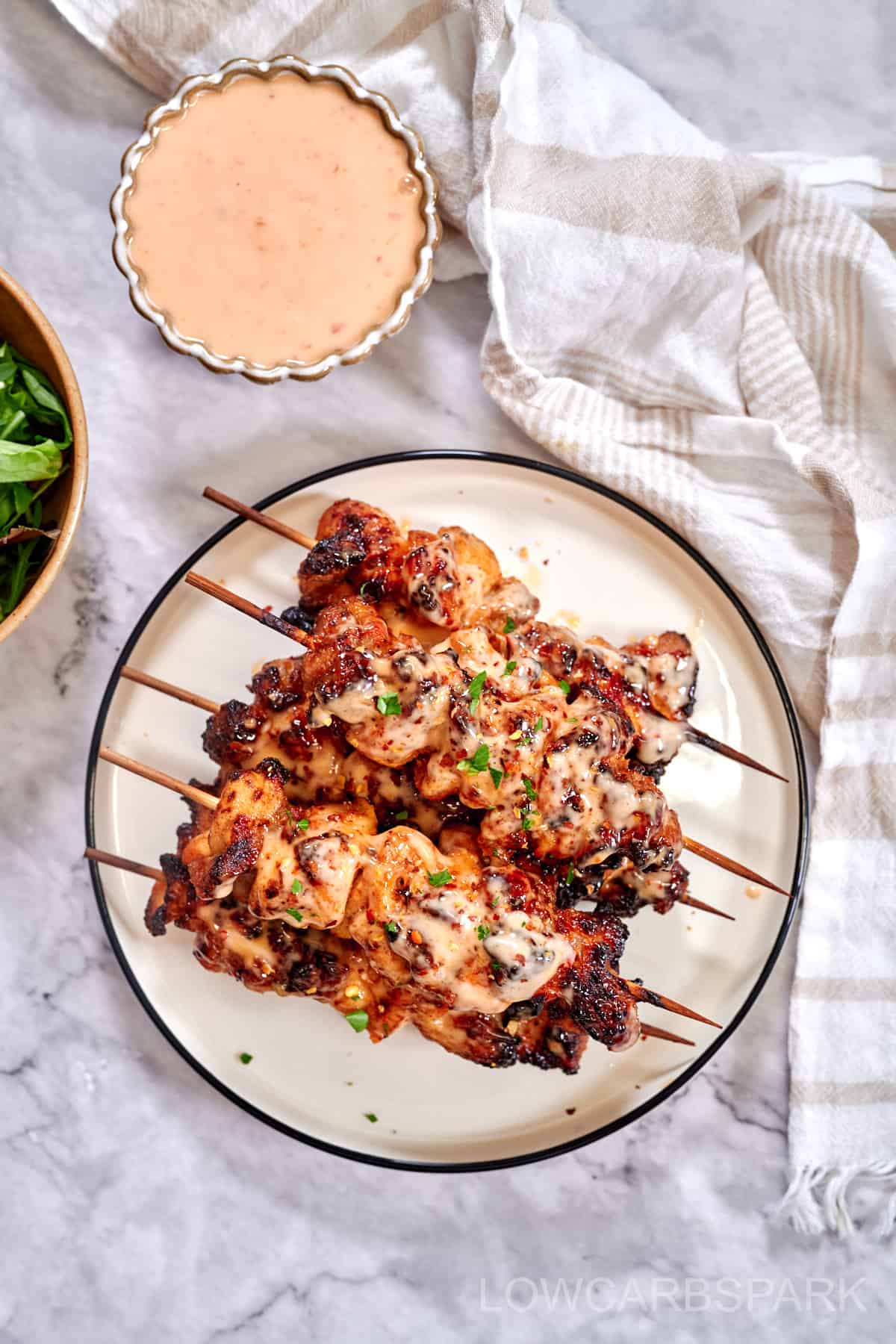 Bang Bang Chicken Skewers on a plate on a marble table with a bowl of dipping sauce.