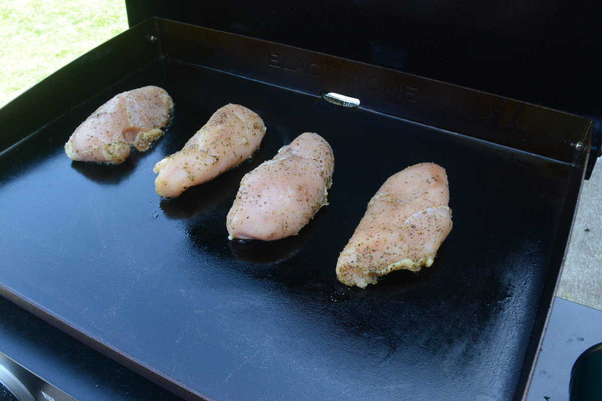 Four uncooked chicken breast pieces with seasoning on a griddle 