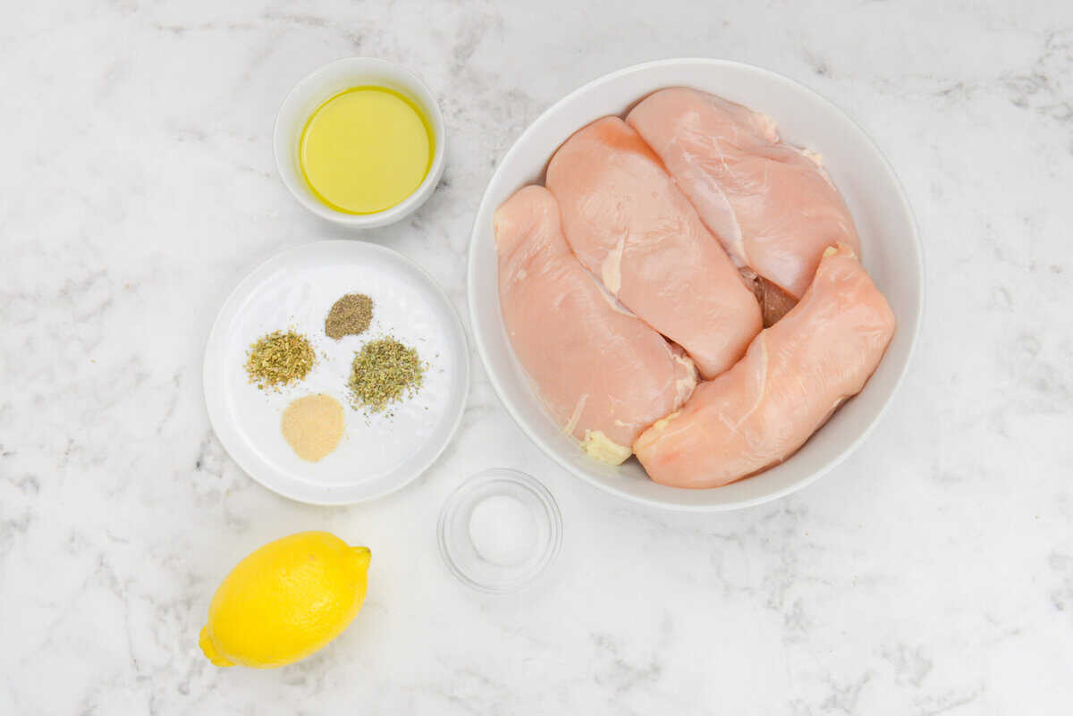 The ingredients to make Blackstone Chicken breast are placed in small bowls next to the raw chicken. The spices are placed on a small white plate
