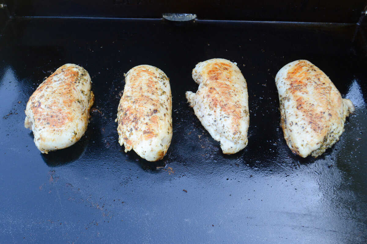 Four pieces of chicken breast are fully cooked and browned sit on top of the Blackstone griddle surface
