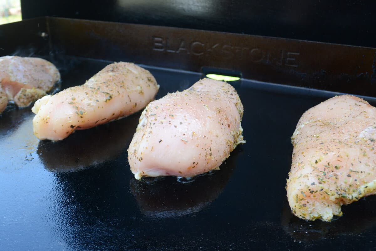 Three pieces of raw chicken breast is placed on the griddle