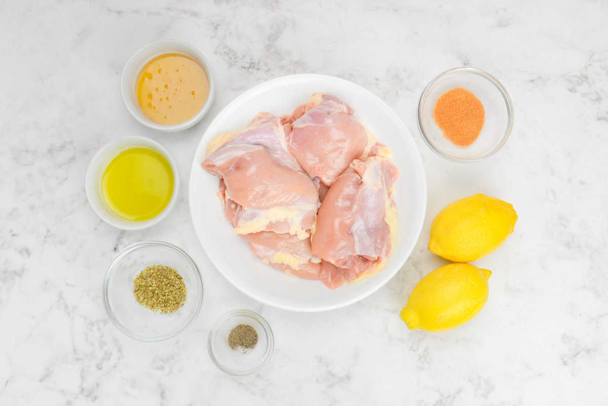 Raw chicken thighs are placed on a plate and surrounded by the ingredients to make the recipe in small bowls.