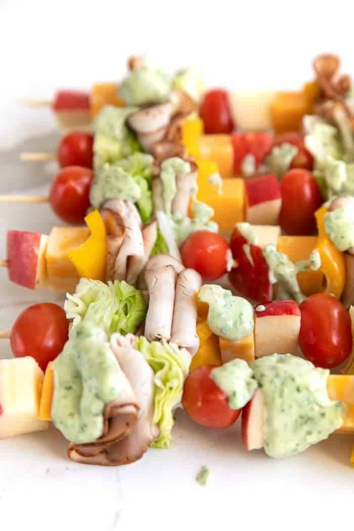 Deli meats, tomatoes, cheese, and sauce on wooden skewers.