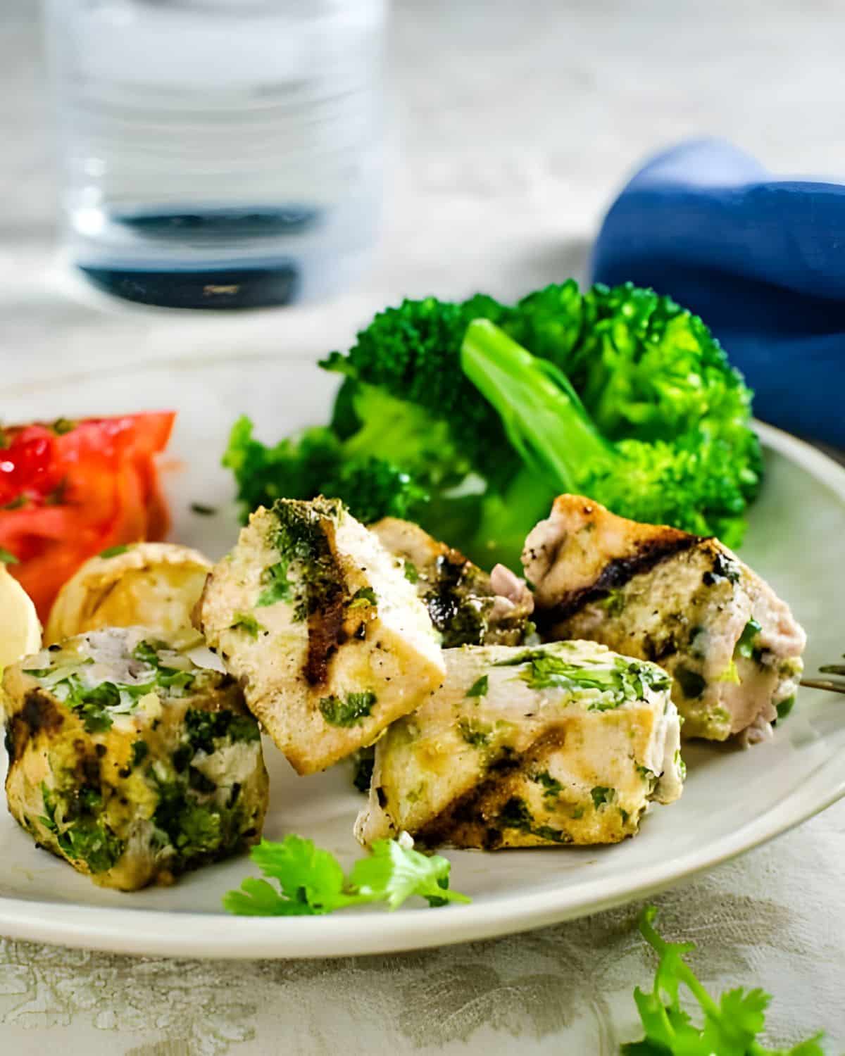 Grilled white fish with herbs with broccoli and tomatoes on a plate.