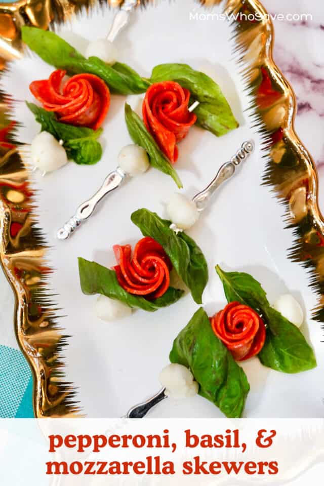 Pepperoni, mozzarella balls, and basil in the shape of rose buds with skewers in them on a tray.