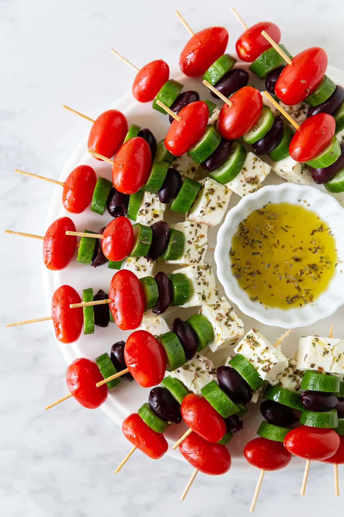 Tomatoes, cucumbers, olives, and feta cheese on a tray with a dipping sauce.