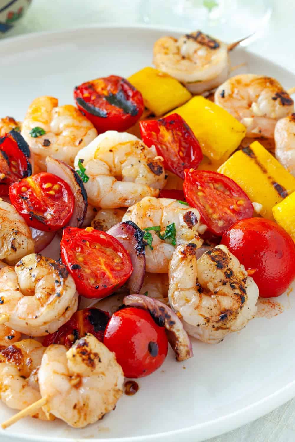 Grilled shrimp, tomatoes, and vegetables on skewers on a plate on a table.