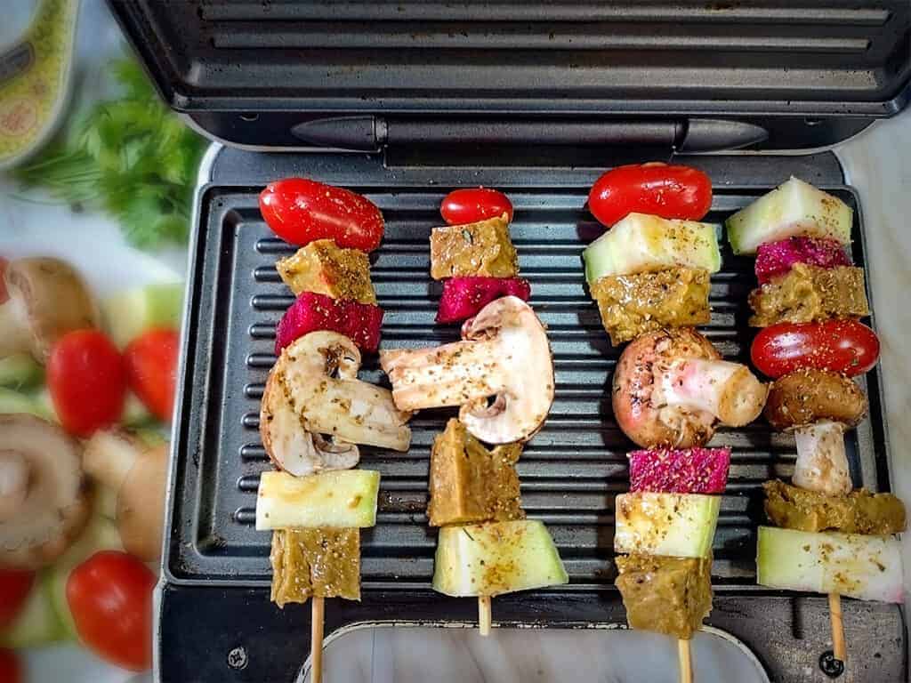 Mushrooms and vegetables on skewers on a mini grill.