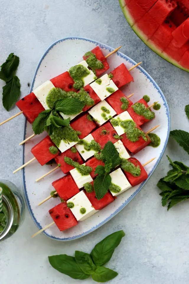 Watermelon, feta cheese, and mint on skewers on a serving plate on a table.