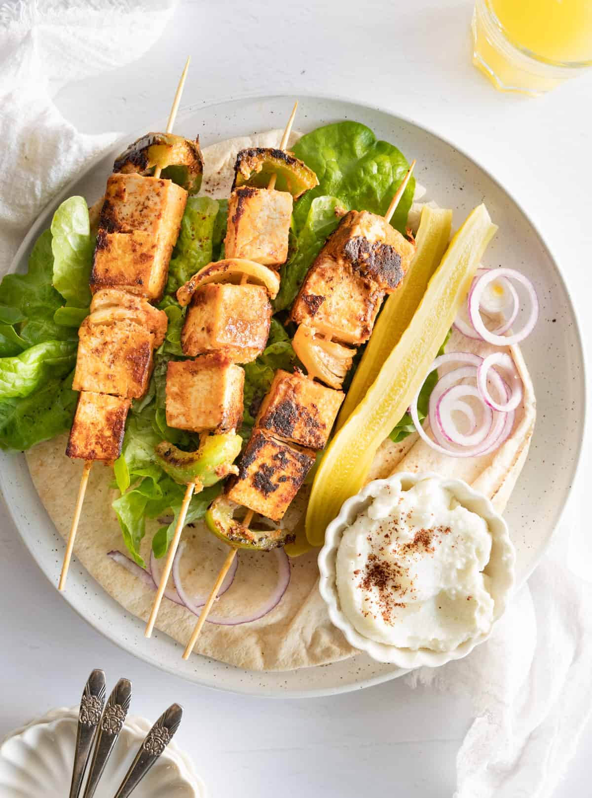 Grilled tofu and vegetables on a plate with lettuce, cheese, onions, and a dipping sauce.