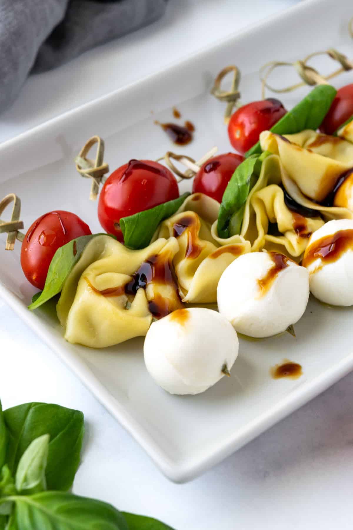 Tomatoes, basil, tortellini, and mozzarella balls on wooden skewers on a serving plate.