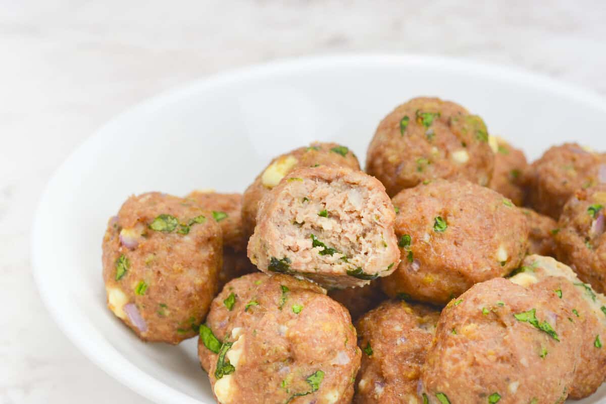 A white bowl filled with baked meatballs in a small pile. One of the meatballs has a bite taken out.