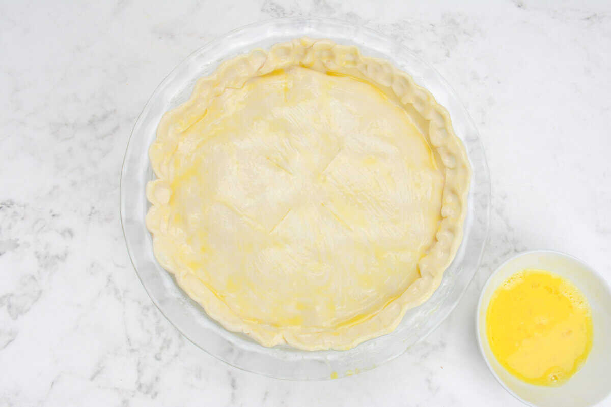 The finished but unbaked chicken pot pie is shown with a yellow egg wash coating the crust 