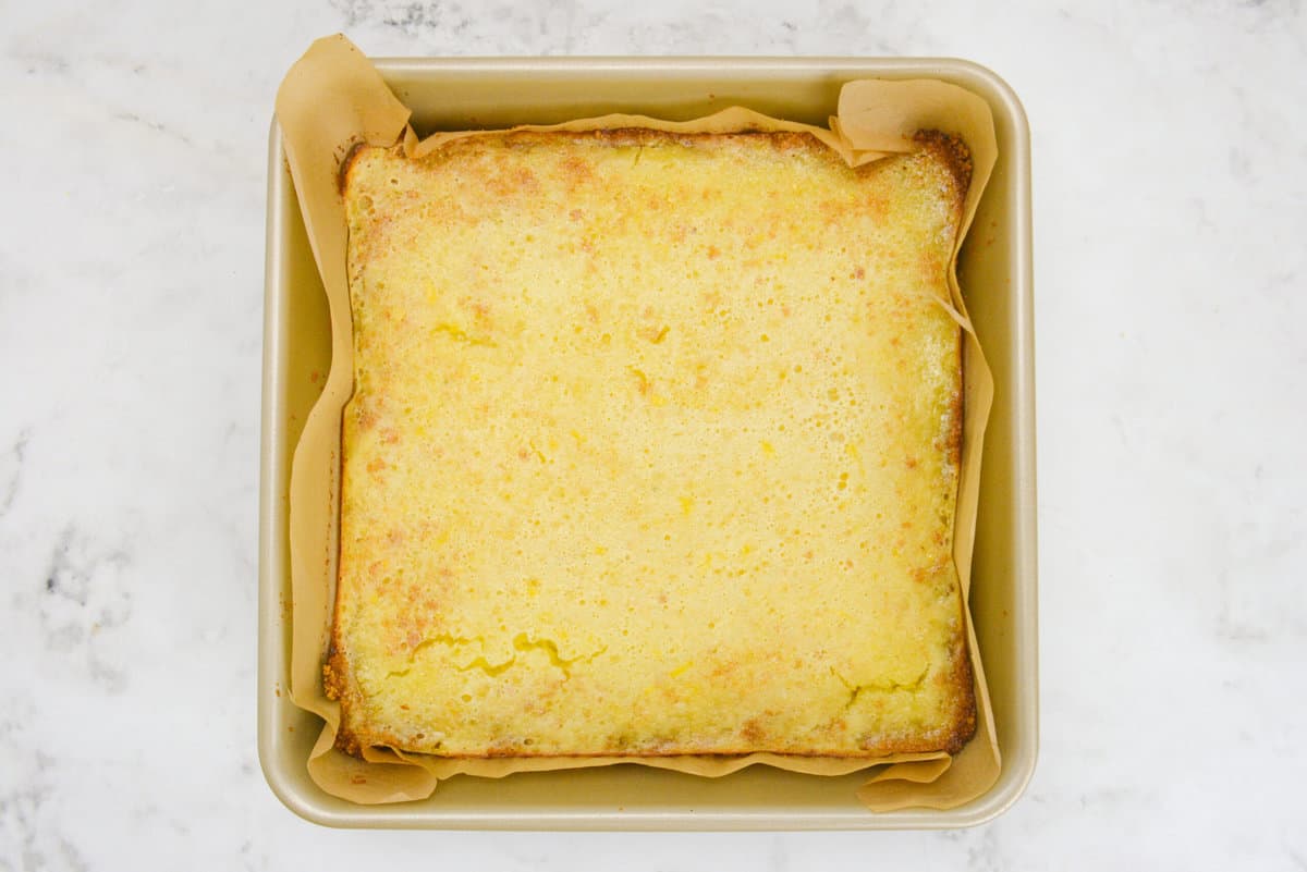 A gold pan with the baked lemon bars. The edges are browned and speckles of grahams dot the lemon curd