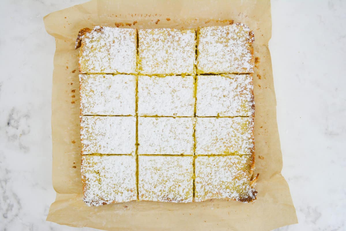 The finished bars topped with powdered sugar shown sliced into 12 equal bars on top of brown parchment 