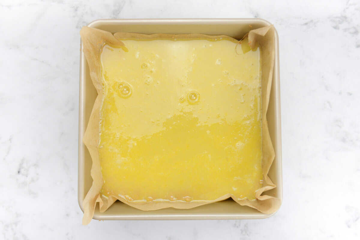 A gold baking pan with the yellow filling on top of the crust before baking