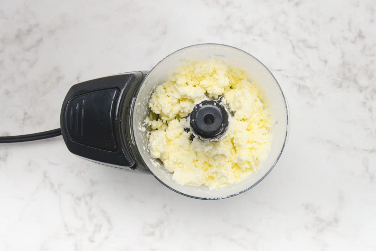 A small food processor shows the texture after the initial blend of feta.