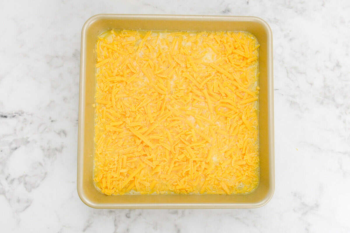 A gold baking pan is filled with the unbaked but completed casserole and topped with shredded cheese