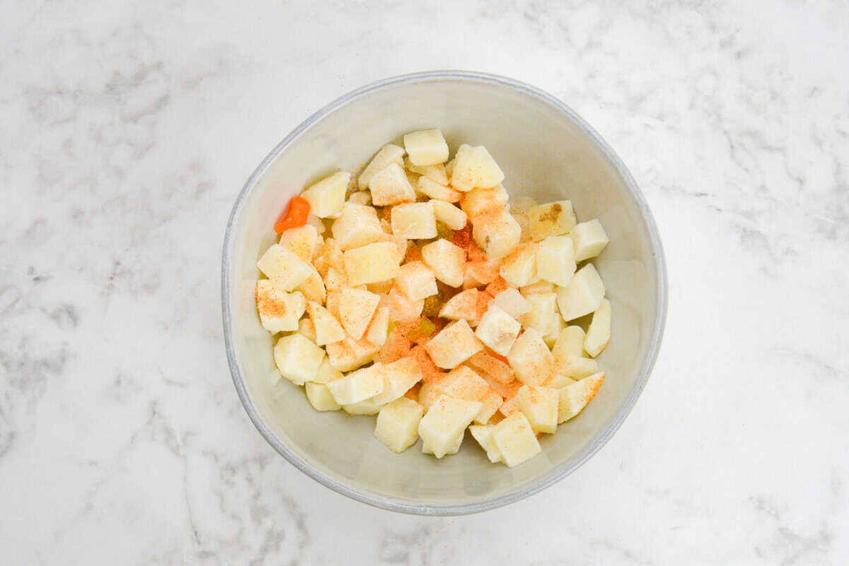 A bowl half filled with frozen potatoes that have seasoned salt sprinkled over them.
