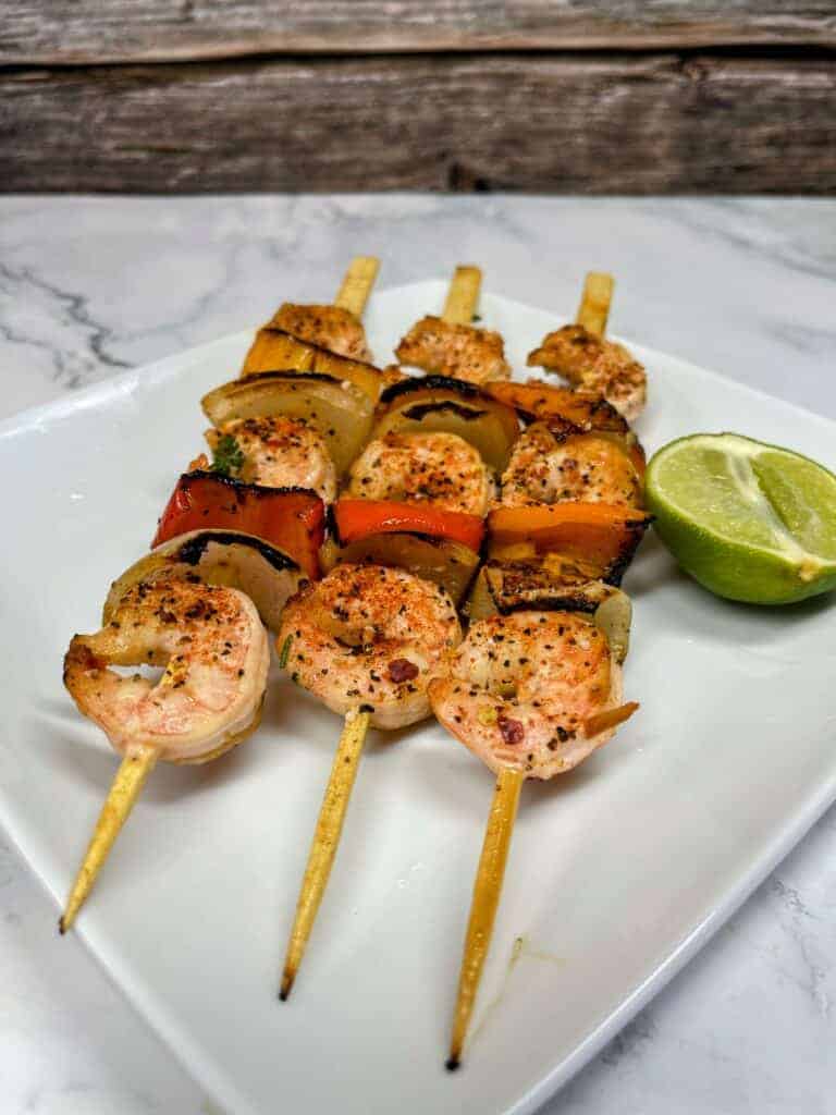 Shrimp and vegetables on skewers on a square plate with a piece of lime.