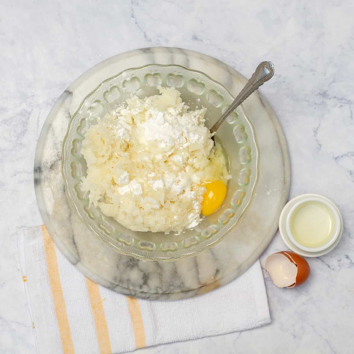 A mixing bowl with the grated cooked yuca, egg, cassava flour, cottage cheese, and salt