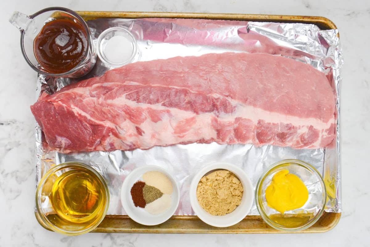 All of the ingredients to make Blackstone ribs are placed on a large baking tray in various sized bowls.