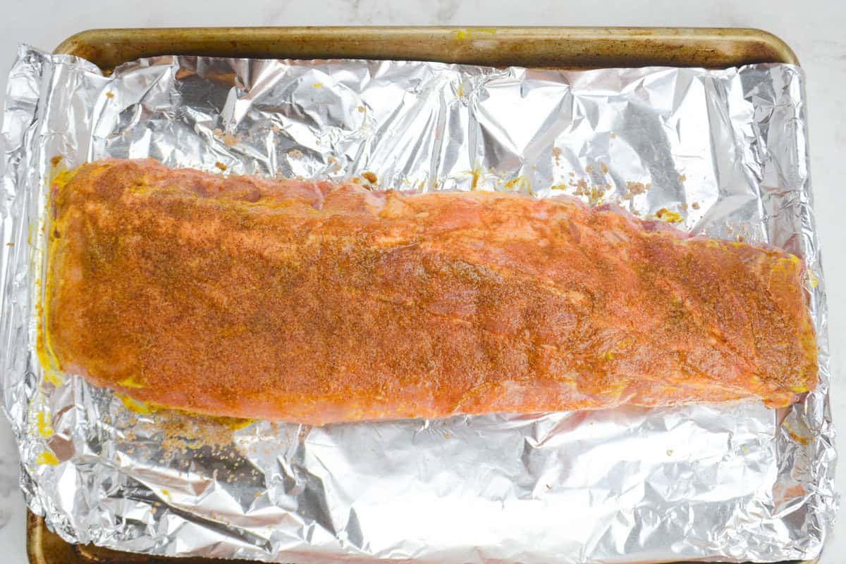 A large baking sheet lined in foil. The uncooked ribs are light brown from the dry rub 