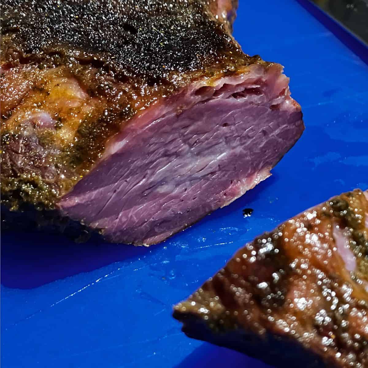 Slicing smoked tri tip on blue cutting board after resting for 30 minutes. 