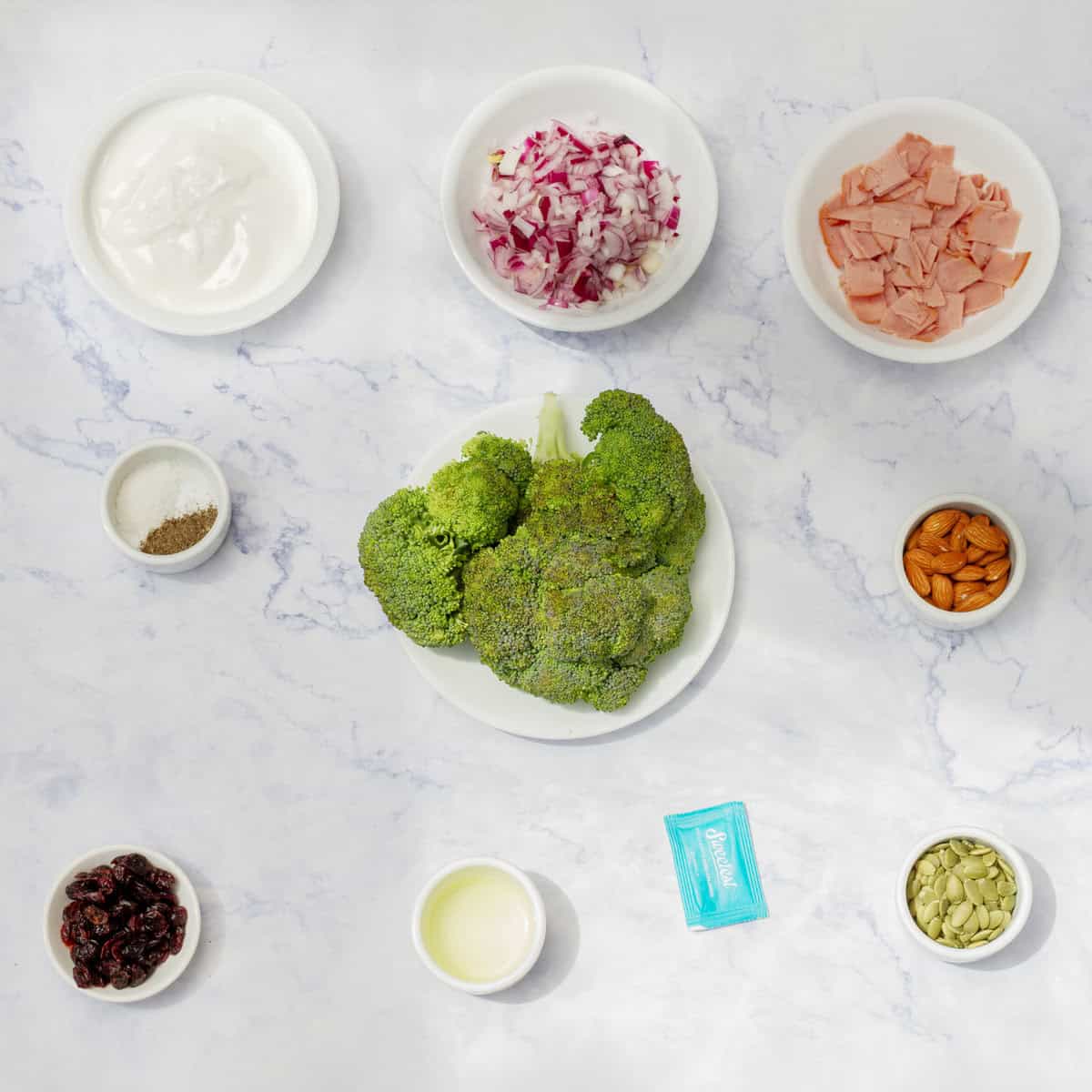 Broccoli salad ingredients of raw broccoli, chopped ham, red onion, dried cranberries, chopped nuts, Greek yogurt, and seasonings. 