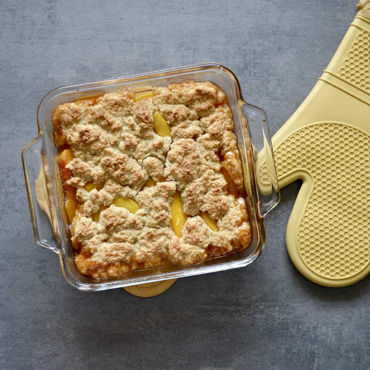 Baking dish with peach cobbler and oven mitt