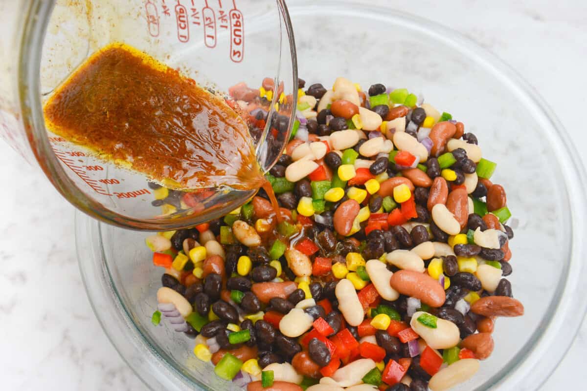 A 45 degree angle close up of the dressing being poured over the Mexican three bean salad 