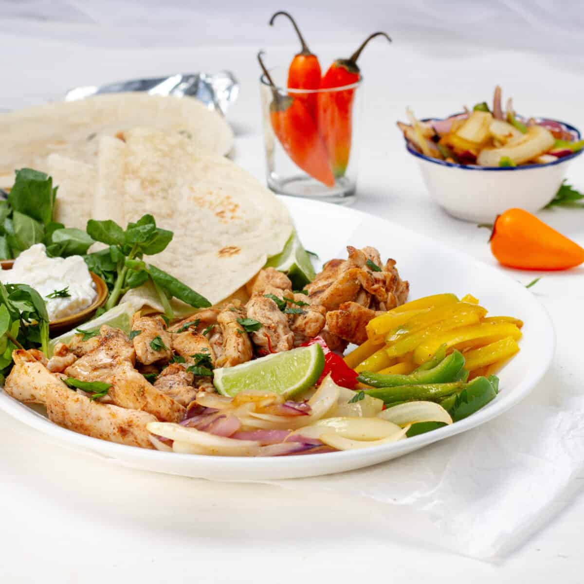 A white plate of Weight Watchers chicken fajitas with grilled peppers, onions, lime and flour tortillas, ready for a photo log.