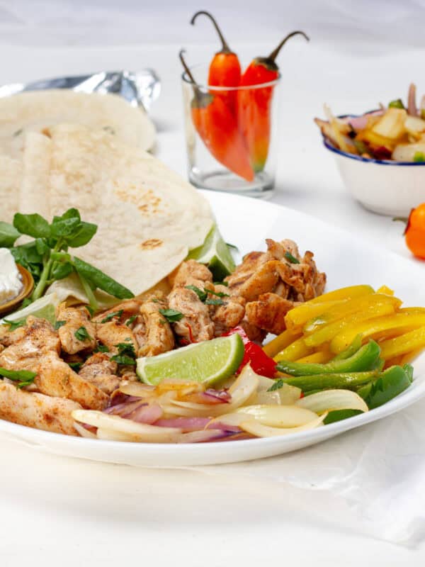 Chicken fajitas with bell pepper and onion on a plate with tortillas.