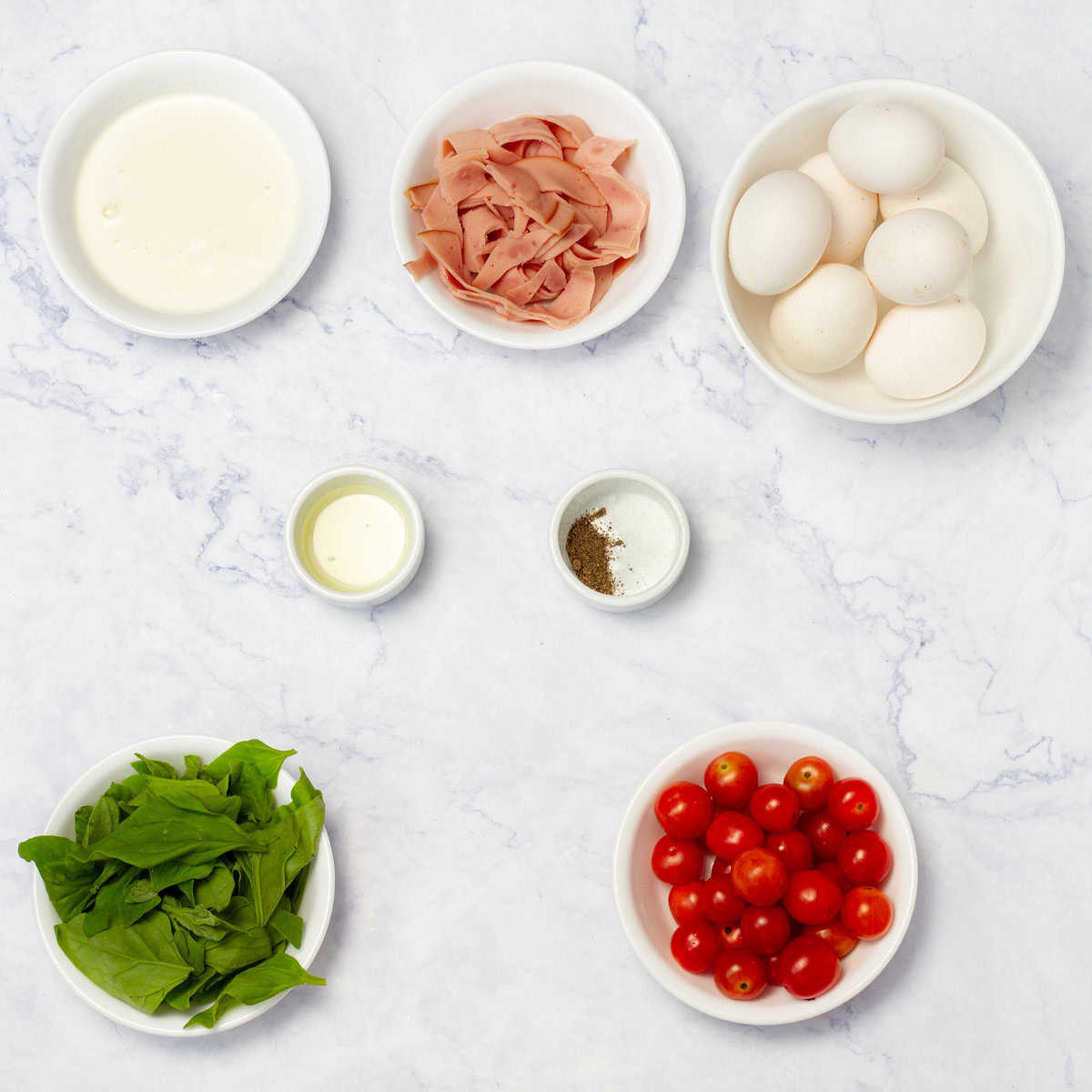 Ingredients of eggs, turkey ham, veggies, and seasonings in separate dishes. 