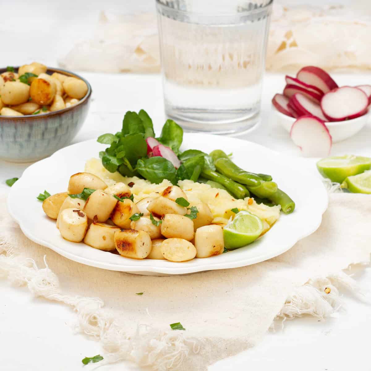 Seared scallops with lemon, garlic and basil on a plate with a green salad and radishes.