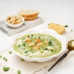 Creamy Pea and Spinach Soup in a bowl with croutons on top and a spoon on the side.