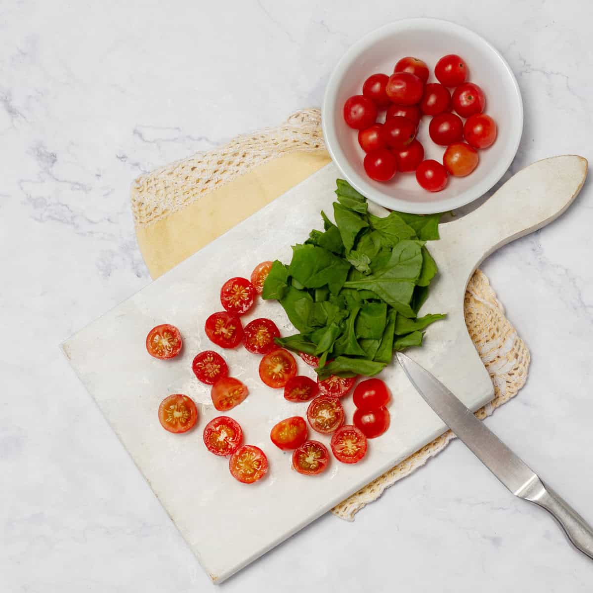 Cherry tomatoes and herbs being chopped on a cutting board. 