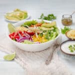The Ultimate Turkey Taco Salad—loaded with veggies, ground turkey, black beans, and a cilantro-lime dressing—in a bowl served with fresh lime wedges.