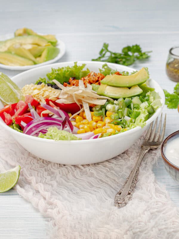 The Ultimate Turkey Taco Salad—loaded with veggies, ground turkey, black beans, and a cilantro-lime dressing—in a bowl served with fresh lime wedges.