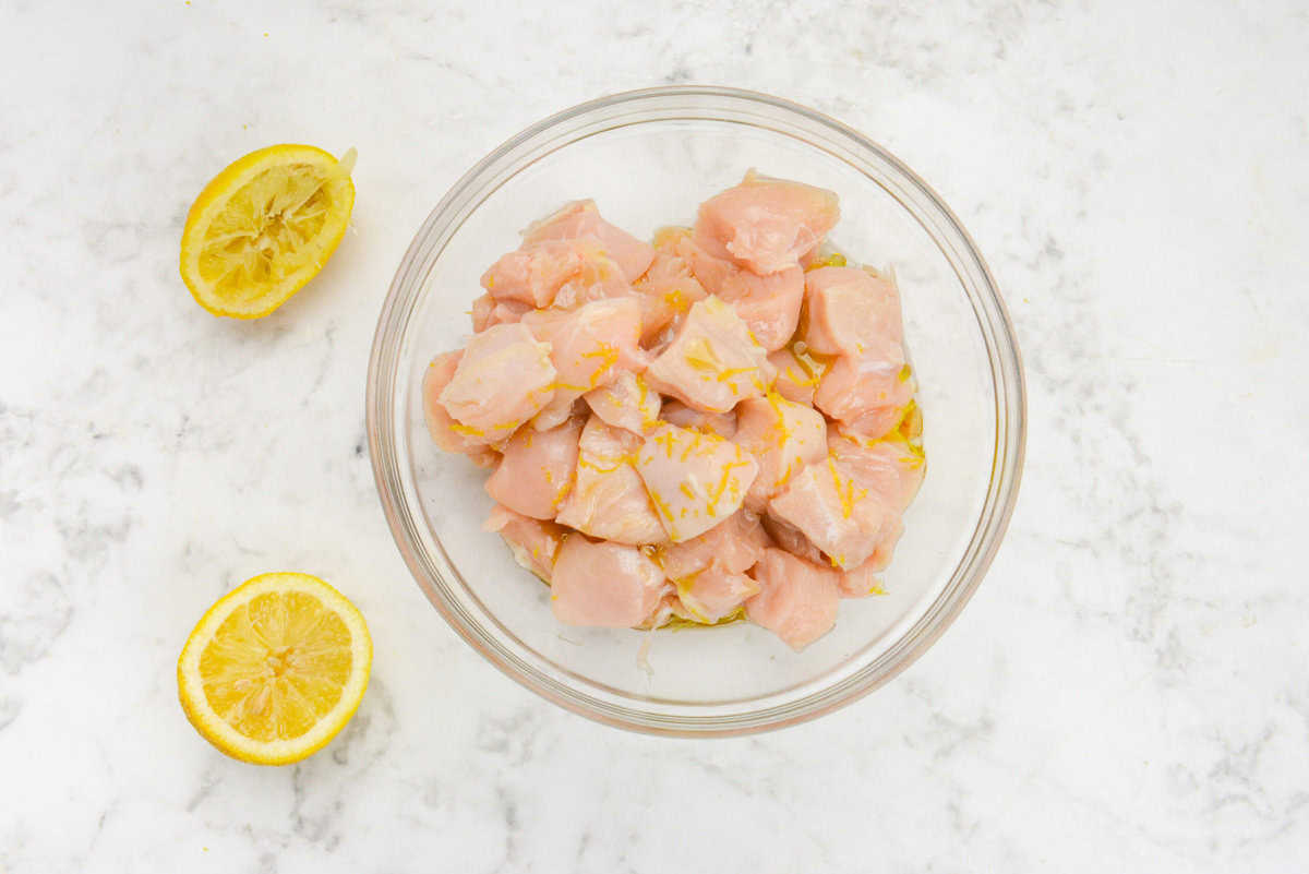 A large clear bowl filled with diced chicken sits beside a cut lemon