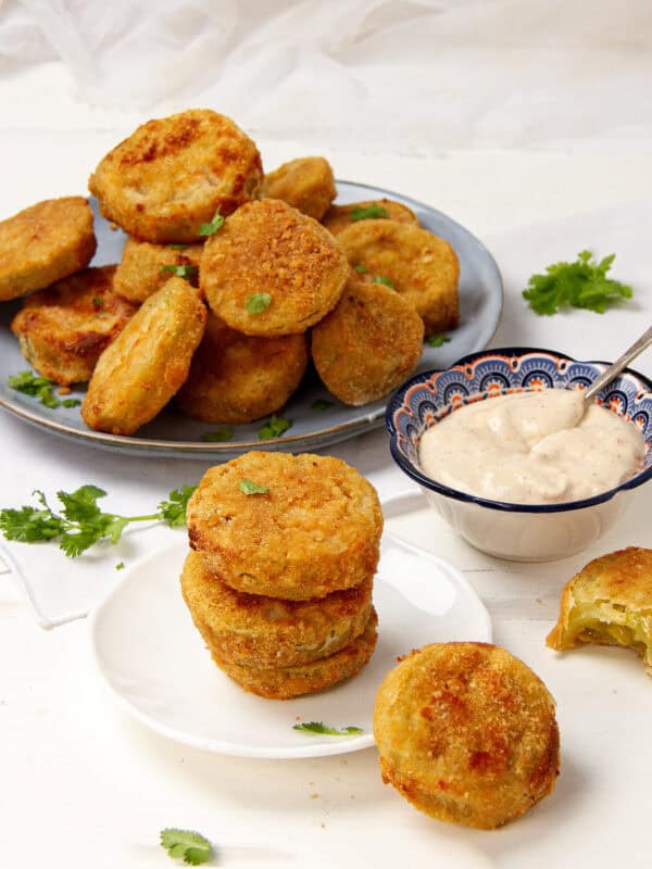 Crispy and delicious fried green tomatoes on a plate with a bowl of dipping sauce on the side.