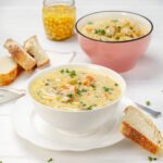 Creamy chicken pasta soup in a bowl with bread on the side.